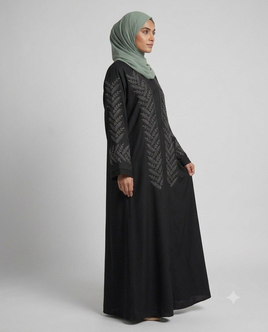 Woman wearing black fern embroidered abaya with sage green hijab, side view