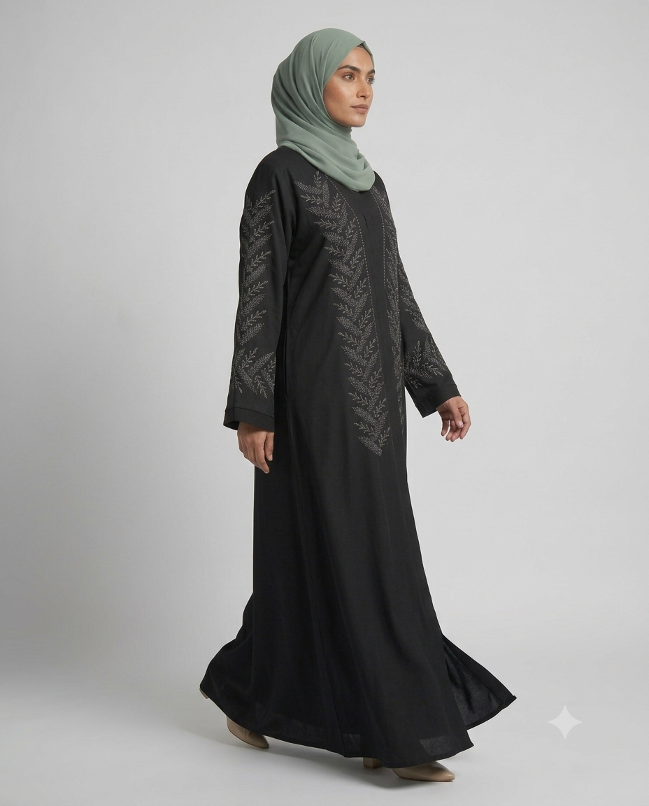 Woman wearing black fern embroidered abaya with sage green hijab, side view