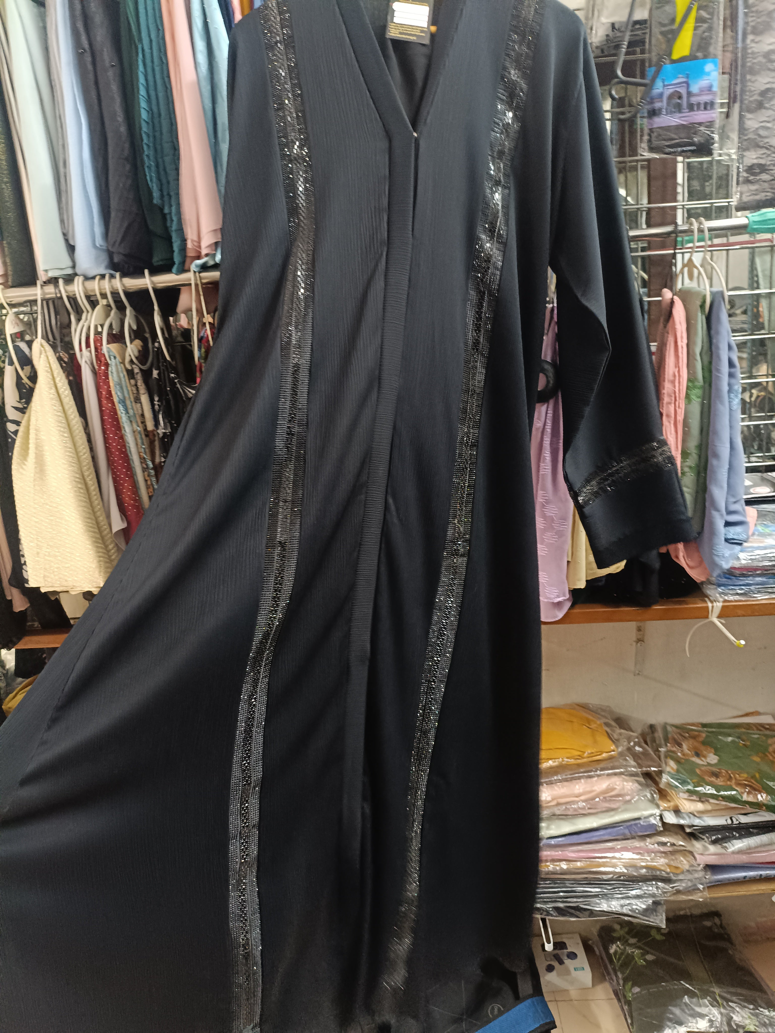 Black open front abaya with black sequin border trim and cuff detail on hanger in store