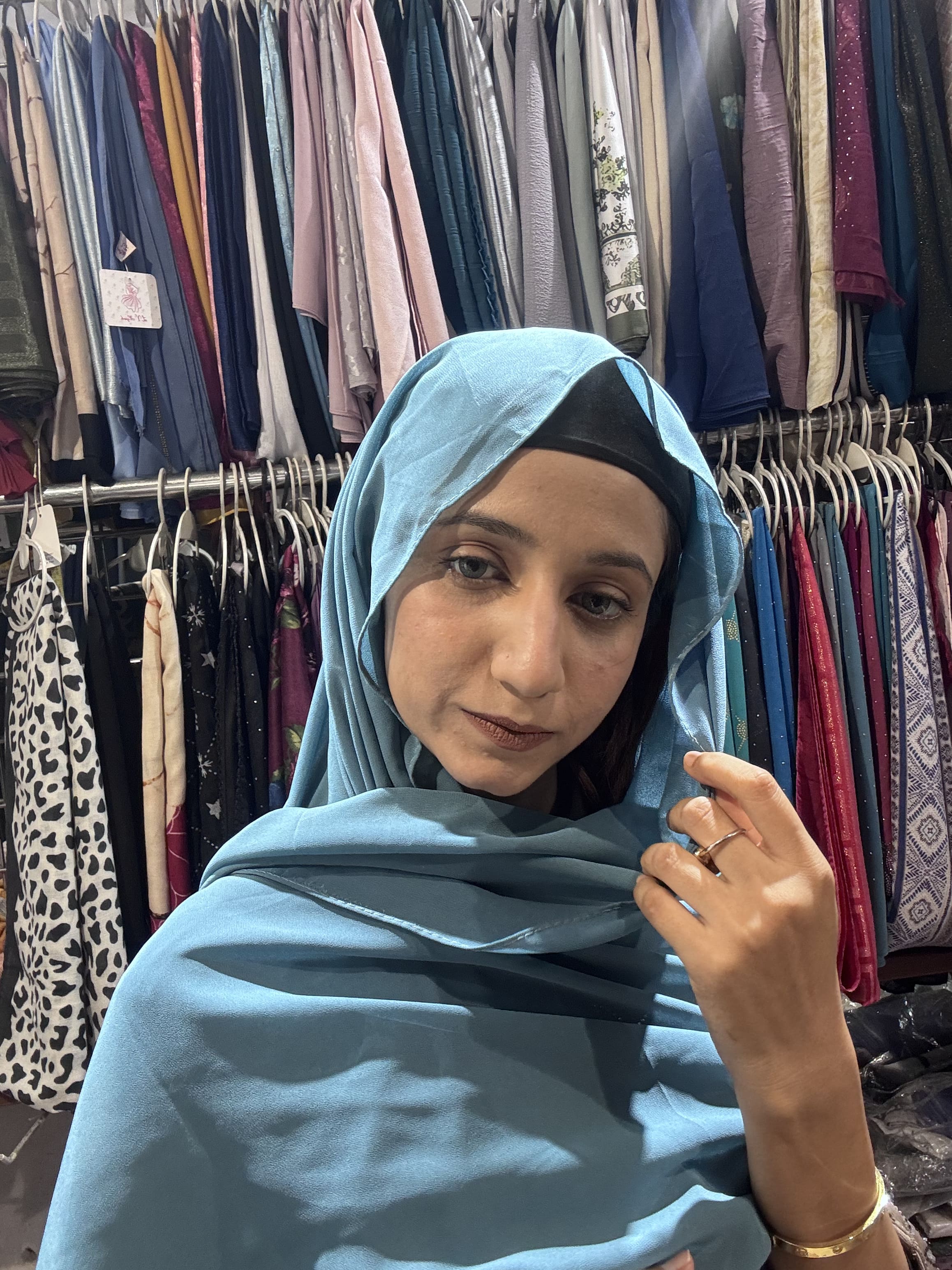 Woman styling cerulean blue premium chiffon hijab scarf in boutique store