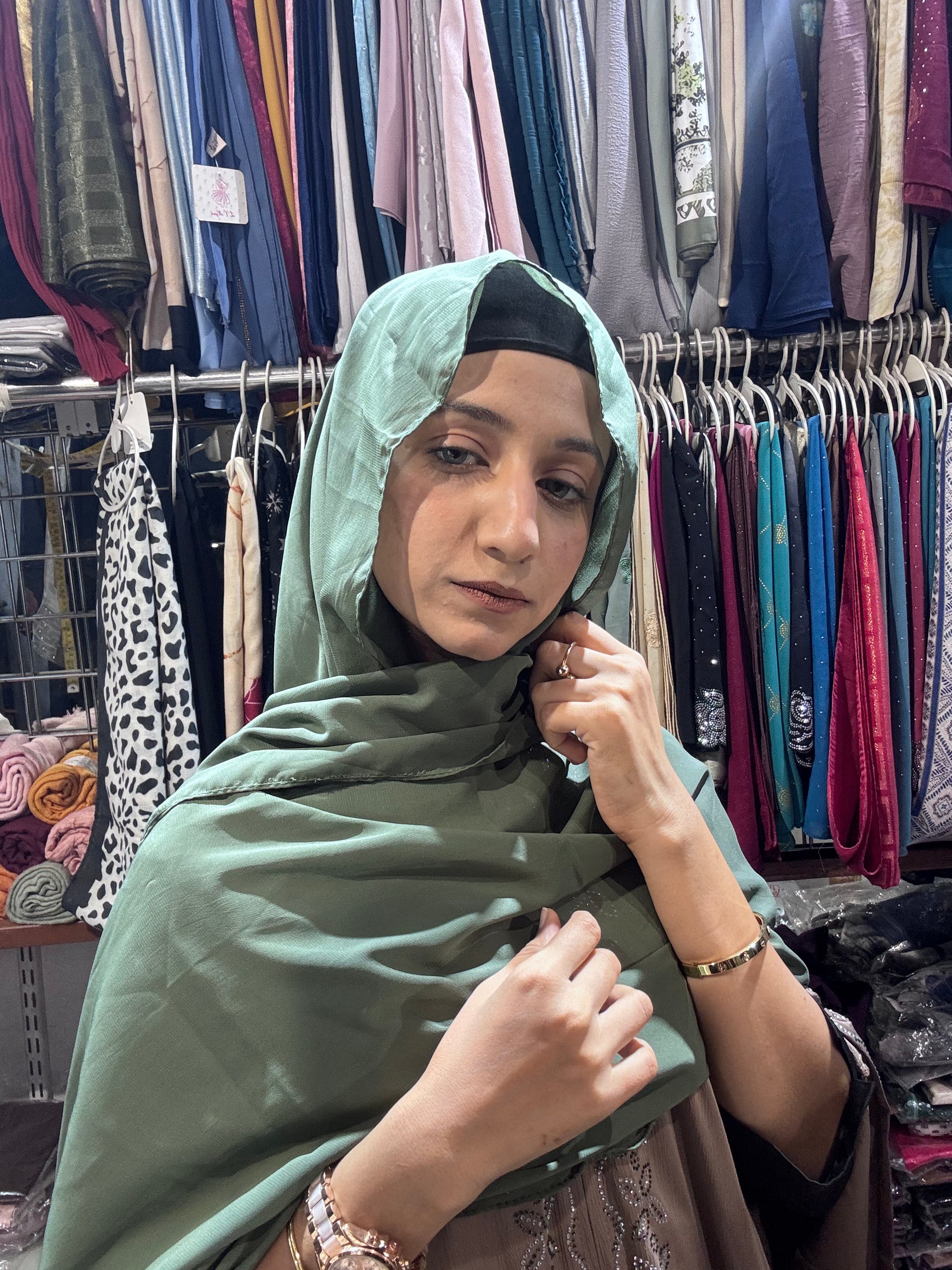 Woman styling olive green premium chiffon hijab scarf in boutique store