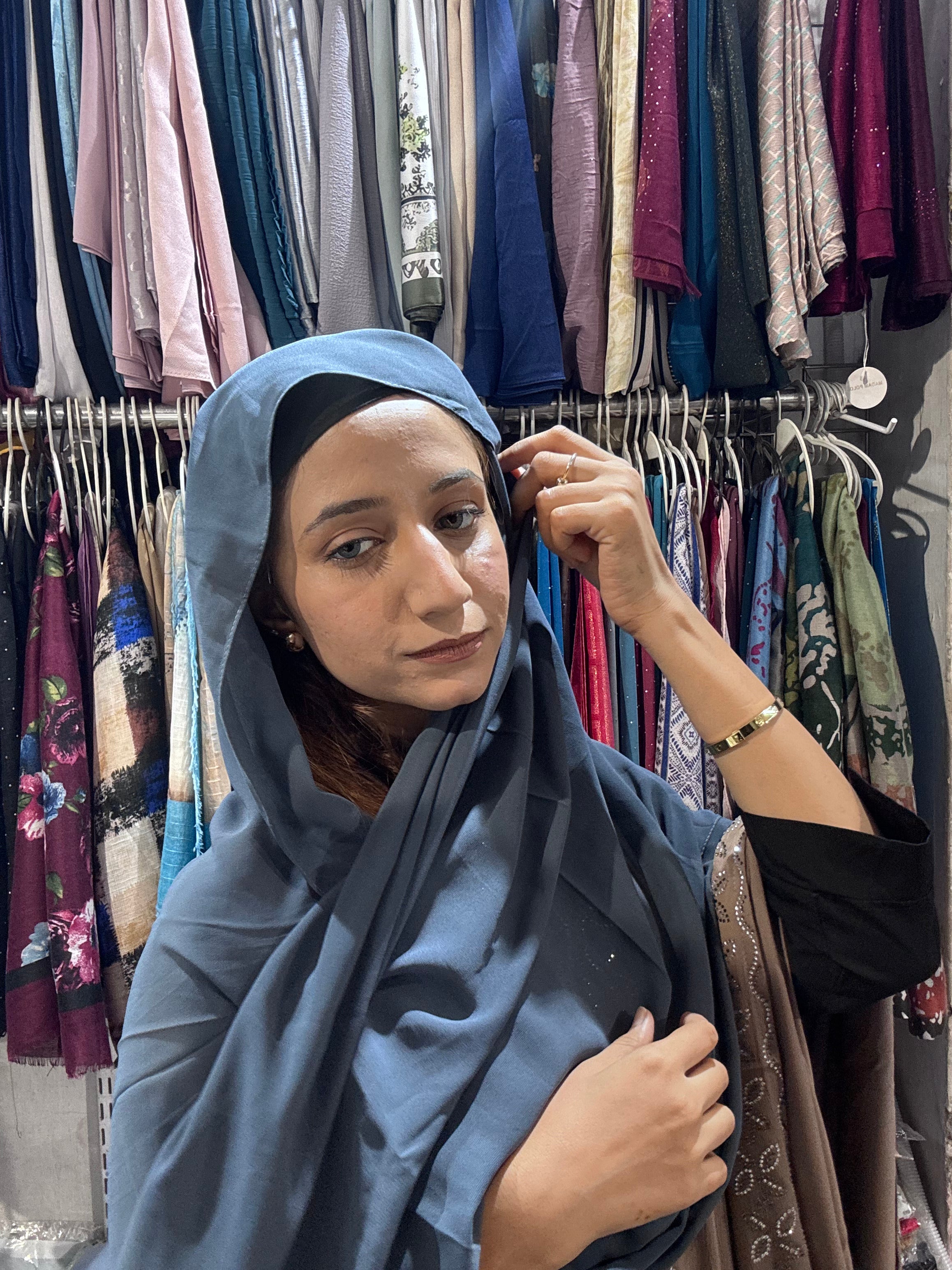 Woman styling steel blue premium chiffon hijab scarf in boutique store